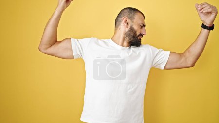 Foto de Joven hombre hispano haciendo un gesto fuerte con los brazos sobre un fondo amarillo aislado - Imagen libre de derechos