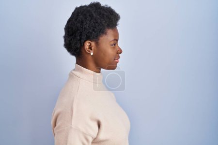 Téléchargez les photos : Femme afro-américaine debout sur fond bleu regardant vers le côté, pose de profil relax avec visage naturel avec sourire confiant. - en image libre de droit