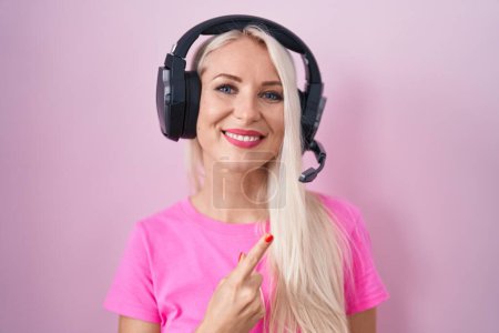 Téléchargez les photos : Femme caucasienne écoutant de la musique à l'aide d'écouteurs gais avec un sourire du visage pointant avec la main et le doigt sur le côté avec une expression heureuse et naturelle sur le visage - en image libre de droit