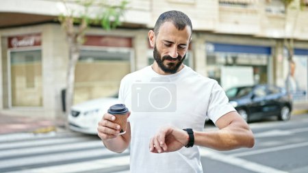 Photo for Young hispanic man drinking coffee looking watch at street - Royalty Free Image