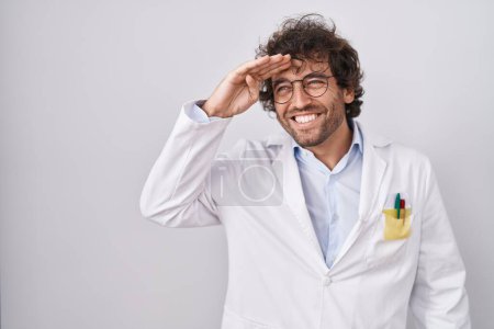 Photo for Hispanic young man wearing doctor uniform very happy and smiling looking far away with hand over head. searching concept. - Royalty Free Image