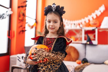 Téléchargez les photos : Adorable fille hispanique portant costume d'Halloween tenant panier de citrouille à la maison - en image libre de droit