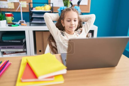 Téléchargez les photos : Adorable étudiante caucasienne utilisant un ordinateur portable détendu avec les mains sur la tête au bureau - en image libre de droit