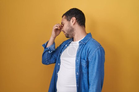 Photo for Hispanic man standing over yellow background tired rubbing nose and eyes feeling fatigue and headache. stress and frustration concept. - Royalty Free Image