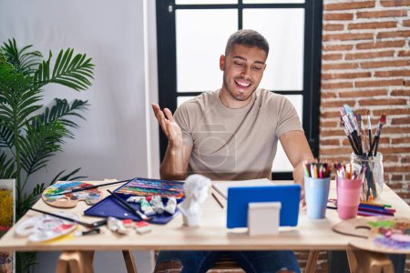 Photo for Young hispanic painter man doing online call with tablet celebrating achievement with happy smile and winner expression with raised hand - Royalty Free Image