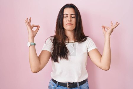 Téléchargez les photos : Jeune femme brune debout sur fond rose détendue et souriante les yeux fermés faisant geste de méditation avec les doigts. concept de yoga. - en image libre de droit