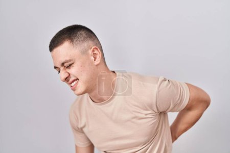 Téléchargez les photos : Jeune homme debout sur fond isolé souffrant de maux de dos, touchant le dos avec la main, douleurs musculaires - en image libre de droit