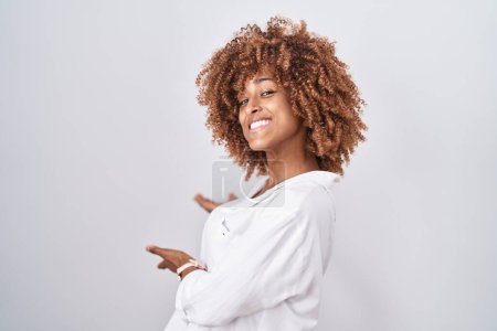 Téléchargez les photos : Jeune femme hispanique aux cheveux bouclés debout sur fond blanc invitant à entrer souriant naturel à la main ouverte - en image libre de droit