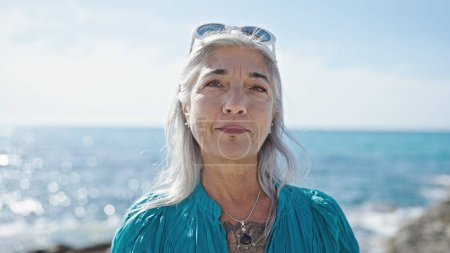 Photo for Middle age grey-haired woman standing with relaxed expression at seaside - Royalty Free Image