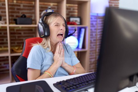 Photo for Young caucasian woman playing video games wearing headphones begging and praying with hands together with hope expression on face very emotional and worried. begging. - Royalty Free Image