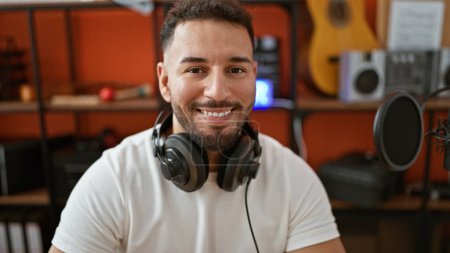 Téléchargez les photos : Jeune homme arabe musicien portant un casque souriant au studio de musique - en image libre de droit