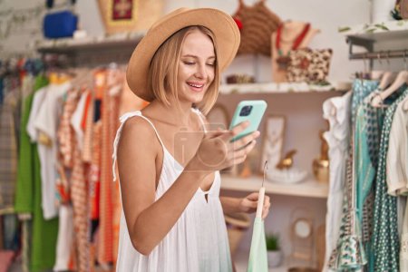 Téléchargez les photos : Young blonde woman customer wearing summer hat using smartphone at clothing store - en image libre de droit