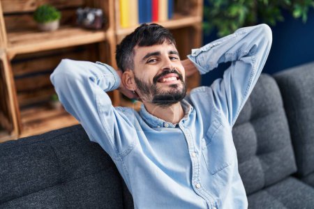 Photo for Young hispanic man relaxed with hands on head sitting on sofa at home - Royalty Free Image