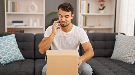 Téléchargez les photos : Jeune homme hispanique parlant au téléphone déballage boîte en carton à la maison - en image libre de droit
