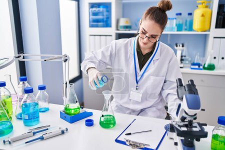 Téléchargez les photos : Jeune femme scientifique mesurant le liquide au laboratoire - en image libre de droit