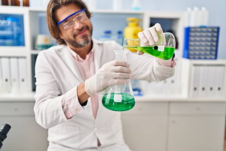 Foto de Hombre científico de mediana edad vertiendo líquido en tubo de ensayo en el laboratorio - Imagen libre de derechos