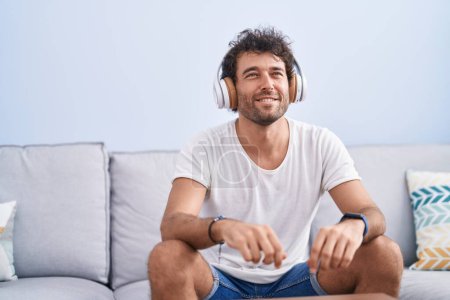 Foto de Joven hispano escuchando música sentado en un sofá en casa - Imagen libre de derechos