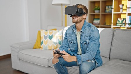 Foto de Joven hombre caucásico jugando videojuego con gafas de realidad virtual y joystick en casa - Imagen libre de derechos