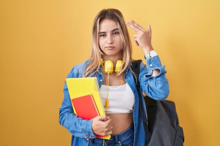 Photo for Young blonde woman wearing student backpack and holding books shooting and killing oneself pointing hand and fingers to head like gun, suicide gesture. - Royalty Free Image