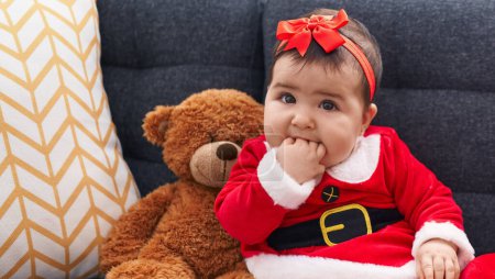 Téléchargez les photos : Adorable bébé hispanique portant le costume de Noël assis sur le canapé à la maison - en image libre de droit