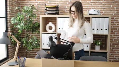 Photo for Young pregnant woman being fired packing belongings from workplace touching belly at office - Royalty Free Image