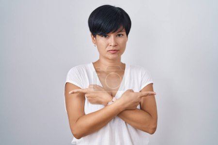 Téléchargez les photos : Jeune femme asiatique avec les cheveux courts debout sur fond isolé pointant vers les deux côtés avec les doigts, direction différente en désaccord - en image libre de droit