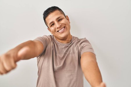 Téléchargez les photos : Jeune homme hispanique debout sur fond blanc approuvant faire un geste positif avec la main, pouces levés souriant et heureux pour le succès. geste gagnant. - en image libre de droit
