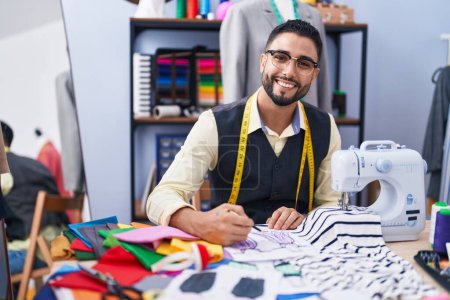 Foto de Joven árabe sastre sonriente dibujo confiado en portátil en la fábrica de ropa - Imagen libre de derechos