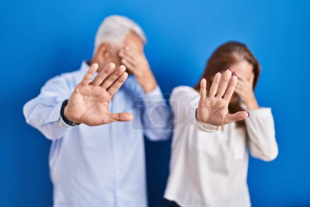 Photo for Middle age hispanic couple standing over blue background covering eyes with hands and doing stop gesture with sad and fear expression. embarrassed and negative concept. - Royalty Free Image