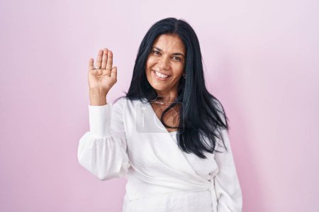 Téléchargez les photos : Femme hispanique mature debout sur fond rose renonçant à dire bonjour heureux et souriant, geste de bienvenue amical - en image libre de droit
