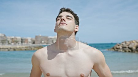 Foto de Hombre joven hispano respirando con expresión relajada en la playa - Imagen libre de derechos