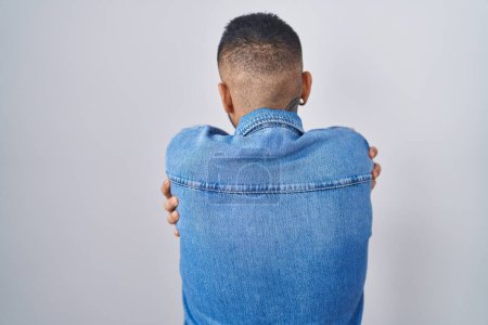 Foto de Joven hombre hispano de pie sobre un fondo aislado abrazándose feliz y positivo desde atrás. amor propio y cuidado personal - Imagen libre de derechos