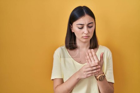 Photo for Hispanic girl wearing casual t shirt over yellow background suffering pain on hands and fingers, arthritis inflammation - Royalty Free Image