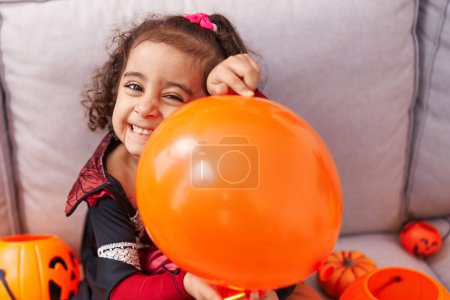 Téléchargez les photos : Adorable fille hispanique portant un costume d'Halloween tenant ballon à la maison - en image libre de droit