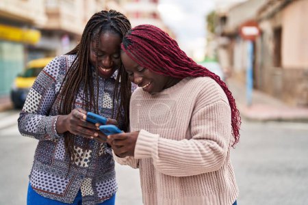 Téléchargez les photos : African american women friends smiling confident using smartphone at street - en image libre de droit