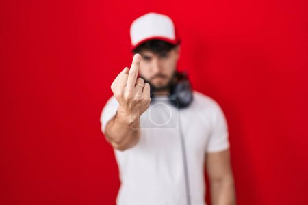 Téléchargez les photos : Hispanic man with beard wearing gamer hat and headphones showing middle finger, impolite and rude fuck off expression - en image libre de droit