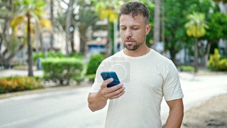 Téléchargez les photos : Jeune homme utilisant un smartphone avec une expression sérieuse au parc - en image libre de droit