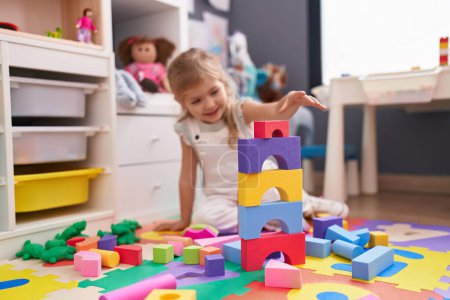 Photo for Adorable blonde girl playing with construction blocks sitting on floor at kindergarten - Royalty Free Image