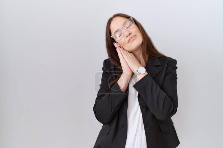Téléchargez les photos : Belle femme brune portant une veste d'affaires et des lunettes dormant fatiguée rêvant et posant les mains ensemble tout en souriant les yeux fermés. - en image libre de droit
