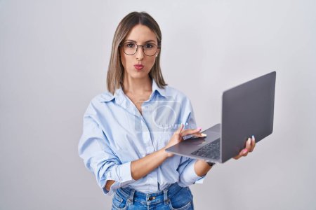 Téléchargez les photos : Jeune femme travaillant à l'aide d'un ordinateur portable en regardant la caméra souffler un baiser sur l'air étant belle et sexy. expression d'amour. - en image libre de droit