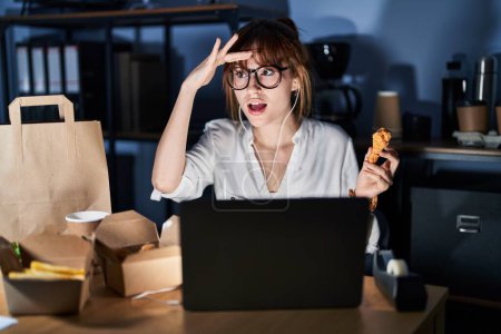 Photo for Young beautiful woman working using computer laptop and eating delivery food very happy and smiling looking far away with hand over head. searching concept. - Royalty Free Image