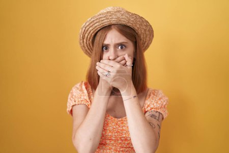 Photo for Young redhead woman standing over yellow background wearing summer hat shocked covering mouth with hands for mistake. secret concept. - Royalty Free Image