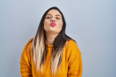Foto de Young hispanic woman standing over isolated background looking at the camera blowing a kiss on air being lovely and sexy. love expression. - Imagen libre de derechos