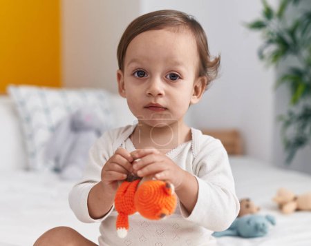 Photo for Adorable hispanic boy sitting on bed holding doll at bedroom - Royalty Free Image