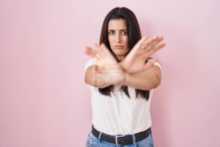 Téléchargez les photos : Jeune femme brune debout sur fond rose expression de rejet croisement des bras et des paumes faisant signe négatif, visage en colère - en image libre de droit