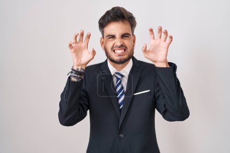 Téléchargez les photos : Jeune homme hispanique avec des tatouages portant un costume d'affaires et une cravate souriant drôle faisant geste griffe comme chat, expression agressive et sexy - en image libre de droit