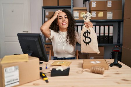 Photo for Young hispanic woman working at small business ecommerce holding money bag stressed and frustrated with hand on head, surprised and angry face - Royalty Free Image