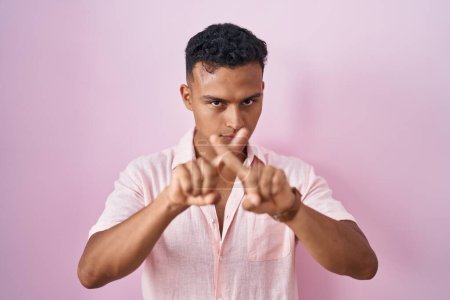 Téléchargez les photos : Jeune homme hispanique debout sur fond rose expression de rejet croisant les doigts faisant signe négatif - en image libre de droit