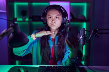 Téléchargez les photos : Jeune femme asiatique jouer à des jeux vidéo avec smartphone couper la gorge avec la main comme couteau, menacer d'agression avec violence furieuse - en image libre de droit
