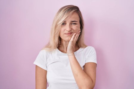 Téléchargez les photos : Young blonde woman standing over pink background touching mouth with hand with painful expression because of toothache or dental illness on teeth. dentist - en image libre de droit